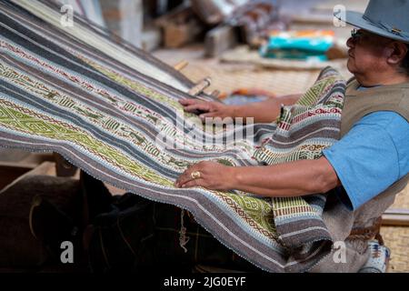 Ecuador, Quito, Paguche. Tahuantinsuyo Weaving Workshop. Traditional "back strap" weaving demonstration. Weaver in typical local attire. Stock Photo