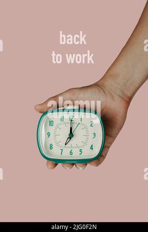 closeup of the hand of a caucasian holding a green alarm clock and the text back to work on a pink background Stock Photo