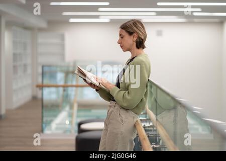 Pensive middle-aged scandinavian woman reading interesting book in library Stock Photo
