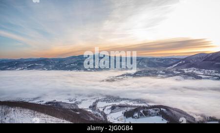 Frosty morning on Skalka mountain in Beskydy mountains overlooking the valley covered with clouds and fog and a view of Lysa mountain. Snowy landscape Stock Photo
