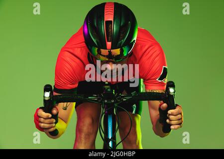 Front camera view of sportsman, cyclist on bicycle in red sports uniform and protective helmet isolated on green background. Stock Photo