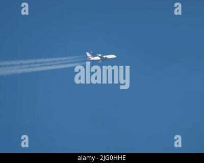 Telephoto view of Emirates Airbus A380 airliner flying at high altitude with contrails Stock Photo