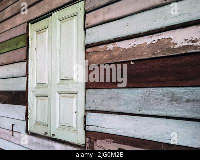 Old grunged wooden window frame painted white vintage with old colourful plywood wall. Antique window frame and old panes. Old closed window and plank Stock Photo