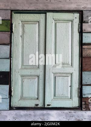 Old grunged wooden window frame painted white vintage with old colourful plywood wall. Antique window frame and old panes. Old closed window and plank Stock Photo