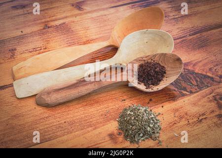 Horizontal photograph of three spoons of three different woods carved by hand with several different spices on a wooden table Stock Photo