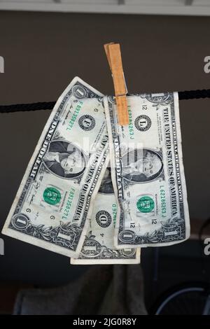 Three American dollar bills pegged hanging on a line against a dark background Stock Photo