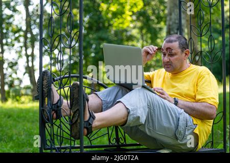 middle aged man with laptop working outside in garden, green home office concept Stock Photo