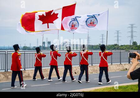 Burlington Teen Tour Band, established in 1947, marches on Lake Ontario Waterfront Trail on Canada Day, July 1, 2022,with skyway and Burlington Canal Lift Bridge in background. Stock Photo