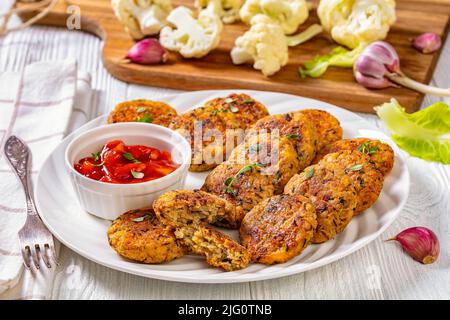 cauliflower patties on white plate with tomato sauce on white textured wooden table, horizontal view from above Stock Photo