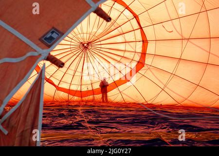 A hot air balloon. The envelope being filled prior to takeoff. A man silhouetted against the rising sun. Stock Photo