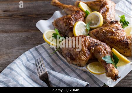Oven baked chicken legs with sliced lemon on a plate isolated on wooden table with copy space Stock Photo