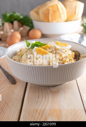 Tuna salad with mayonnaise, boiled eggs and corn in a white bowl. Served with buns Stock Photo