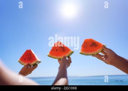 Three hands with watermelon segments are on azure calm sea water background. Stock Photo