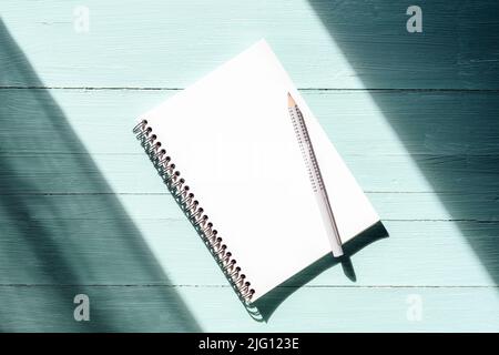 Notepad with blank sheet and pencil on turquoise blue wooden table in sunlight. Top view, flat lay, mockup Stock Photo