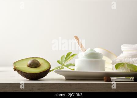 Natural moisturizing cream with avocado extract for skin care with fruits and leaves on white table and white isolated background. Horizontal composit Stock Photo