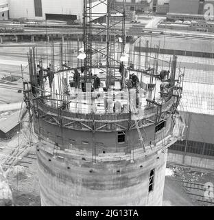 1950s, historical, at the Abbey works site in Port Talbot, Wales, the home of the Steel Company of Wales, a view from above of a tall circular tower made from reinforced concrete under construction. Steel workers on the top....no had hats, just cloth caps! Stock Photo