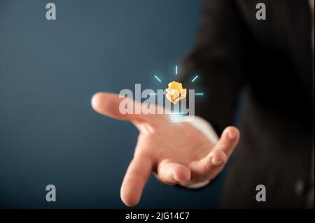 Hand of a businessman presenting a glowing lightbulb on virtual interface in a conceptual image of business idea and innovation. Stock Photo