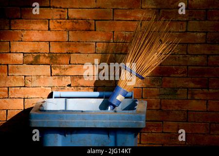 Broom stick in trash cans with brick wall as background Stock Photo