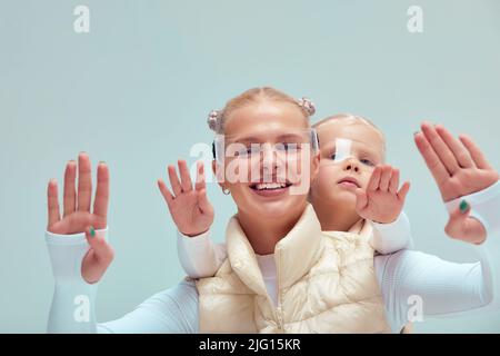 A young woman with her little daughter in a white high-tech clothes wearing smart glasses and pressing by hands up against a holographic screen Stock Photo