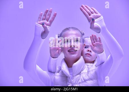 A young woman with her little daughter in a white high-tech clothes wearing smart glasses and pressing by hands up against a holographic screen Stock Photo