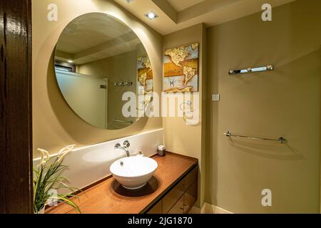 a view from inside a bathroom in front of the sink and a large circular mirror in a apartment along the Costa Del Sol Stock Photo