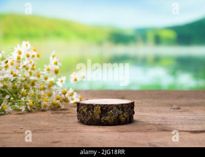 Wooden table with free space for product or composition. Chamomile flowers and empty wooden plate on table by lake (selective focus) Stock Photo