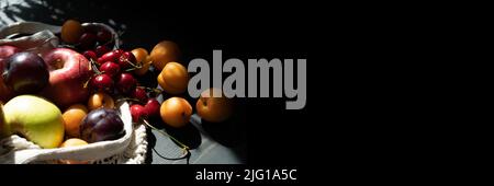 Fresh ripe fruits and berries on a black wooden background in an ecological mesh bag. Lifestyle. Hard shadows. Copy space. Stock Photo