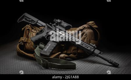 A modern automatic carbine with a collimator sight. The weapon lies on a military backpack. Rifle for the police, special forces or the army. Dark bac Stock Photo