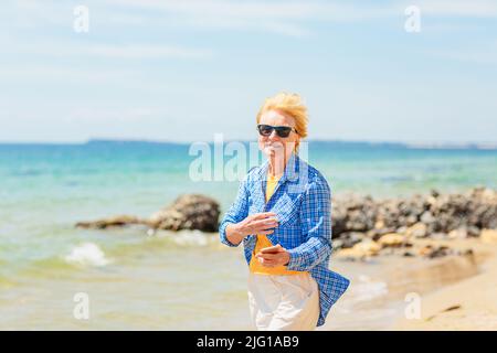 Elderly woman standing on the beach and holding mobile phone. Stock Photo
