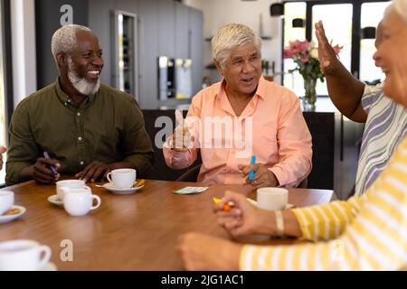 Multiracial happy senior man showing thumbs up while playing bingo with friends at dining table Stock Photo