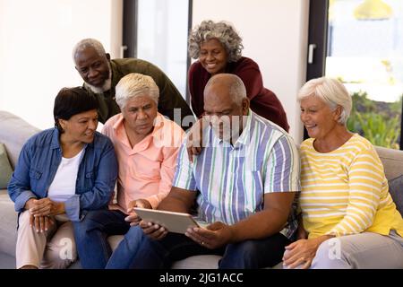 Multiracial curious seniors looking at male friend using digital tablet while sitting on sofa Stock Photo