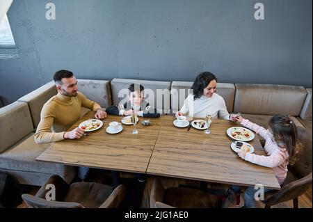 Happy multu-ethnic family having breakfast together in the international airport departure terminal restaurant while waiting to board the flight. Air Stock Photo