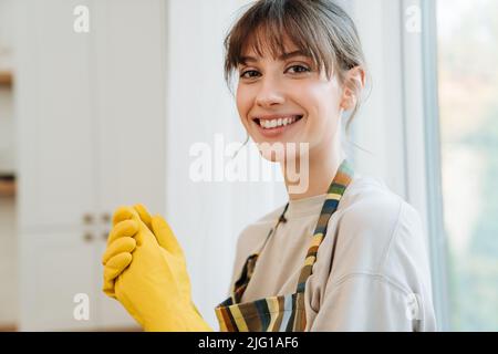 White young woman in gloves smiling while doing housework at home Stock Photo