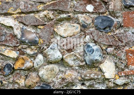 Flushwork flint church wall infilled with fragments of inscribed broken foot stones in red sandstone Stock Photo