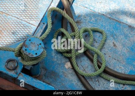 A short length of pale green mooring rope tied to a small single bollard on the deck of a ship painted pale blue Stock Photo