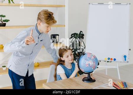 Teenage girl and boy siting near table with globe in classroom. Teen schoolboy and schoolgirl doing project together at school Stock Photo