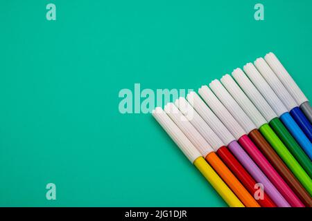 Various markers and colored pencils on a green table. Stock Photo