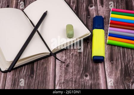 Various school supplies such as markers, colored pens and markers, notebook and eraser. On top of a wooden table. Back to school. Stock Photo