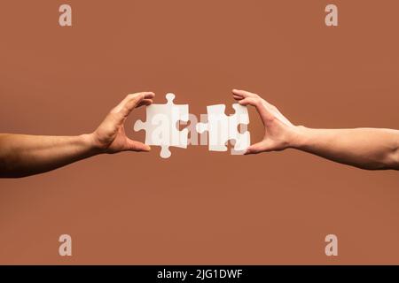Two hands trying to connect couple puzzle piece on blue background ...
