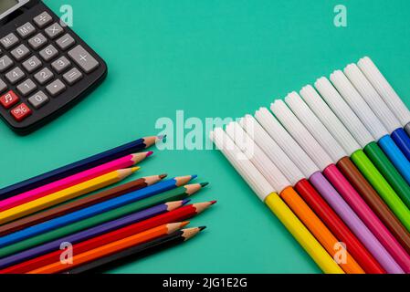 A calculator with several markers and colored pencils on a green table. Back to school. Stock Photo