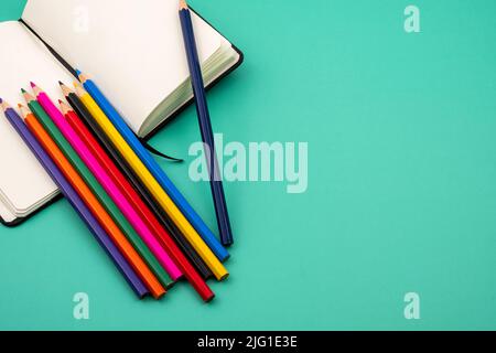 Several colored pencils on top of a notebook on a green table. Back to school. Stock Photo