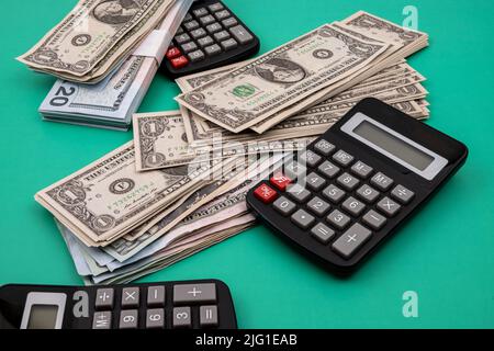 Close-up of a pile of dollar bills, with black calculators, on a green table. Concept of financial calculations. Stock Photo