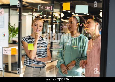 Multiracial female colleagues brainstorming over business plan on glass wall in creative office Stock Photo