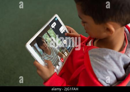 High angle view of biracial boy looking at teacher on digital tablet screen teaching in online class Stock Photo