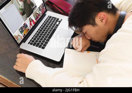 High angle view of teenage asian boy sleeping in front of laptop during online class at home Stock Photo
