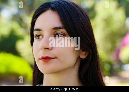Young caucasian woman wearing tee standing on city park, outdoors thinking of problems and feeling lack of energy. Unmotivated lady looking forward. Stock Photo