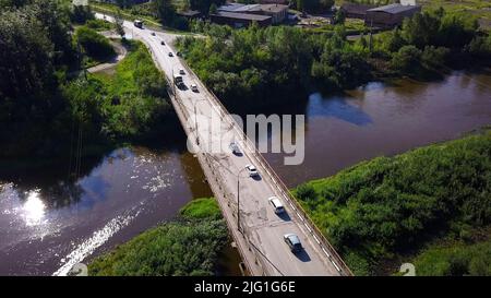 Aerial view of a bridge with driving cars above the river and green nature. Clip. Concept of transportation, bridge in countryside area on a summer su Stock Photo