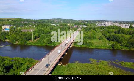 Aerial view of a bridge with driving cars above the river and green nature. Clip. Concept of transportation, bridge in countryside area on a summer su Stock Photo