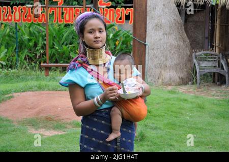 Long-neck woman Padaung tribe (Kayan Lahwi), feeding baby. Pattaya, Thailand Stock Photo