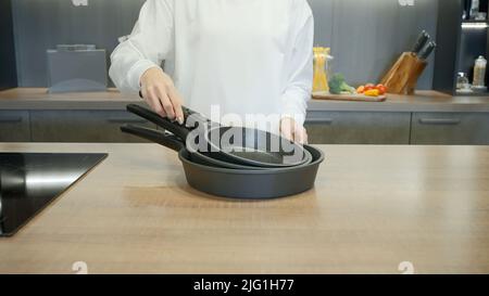 New set of frying pans demonstrated by a chef in white uniform. Action. Interior of a modern kitchen Stock Photo